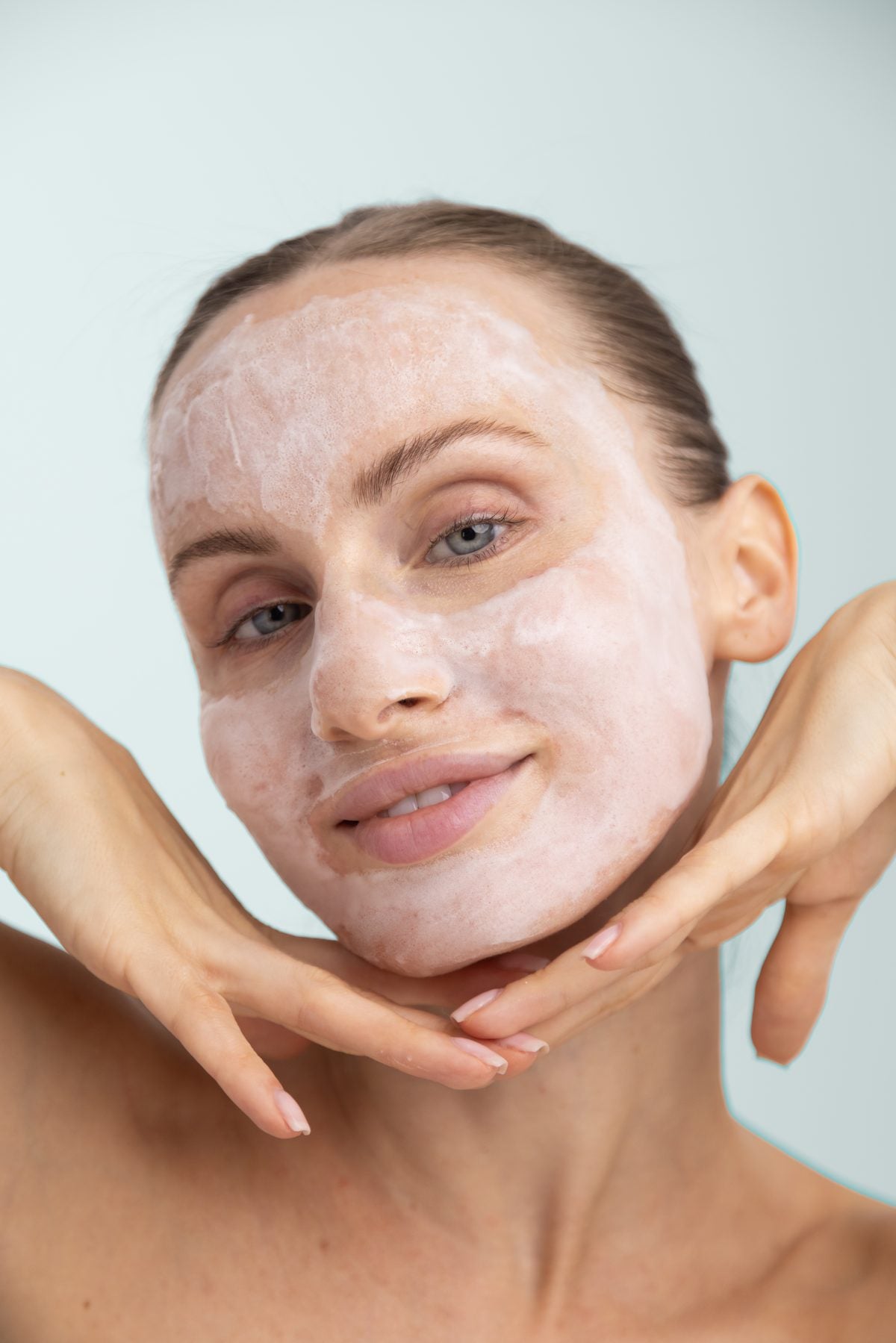Woman with a foaming glow mask on her face, framing her jaw with her hands